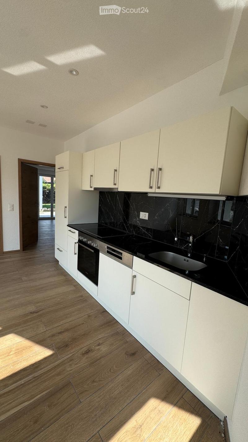 Modern kitchen with white cabinets, black countertops, and a stainless steel sink and oven. Wooden flooring and recessed lighting.