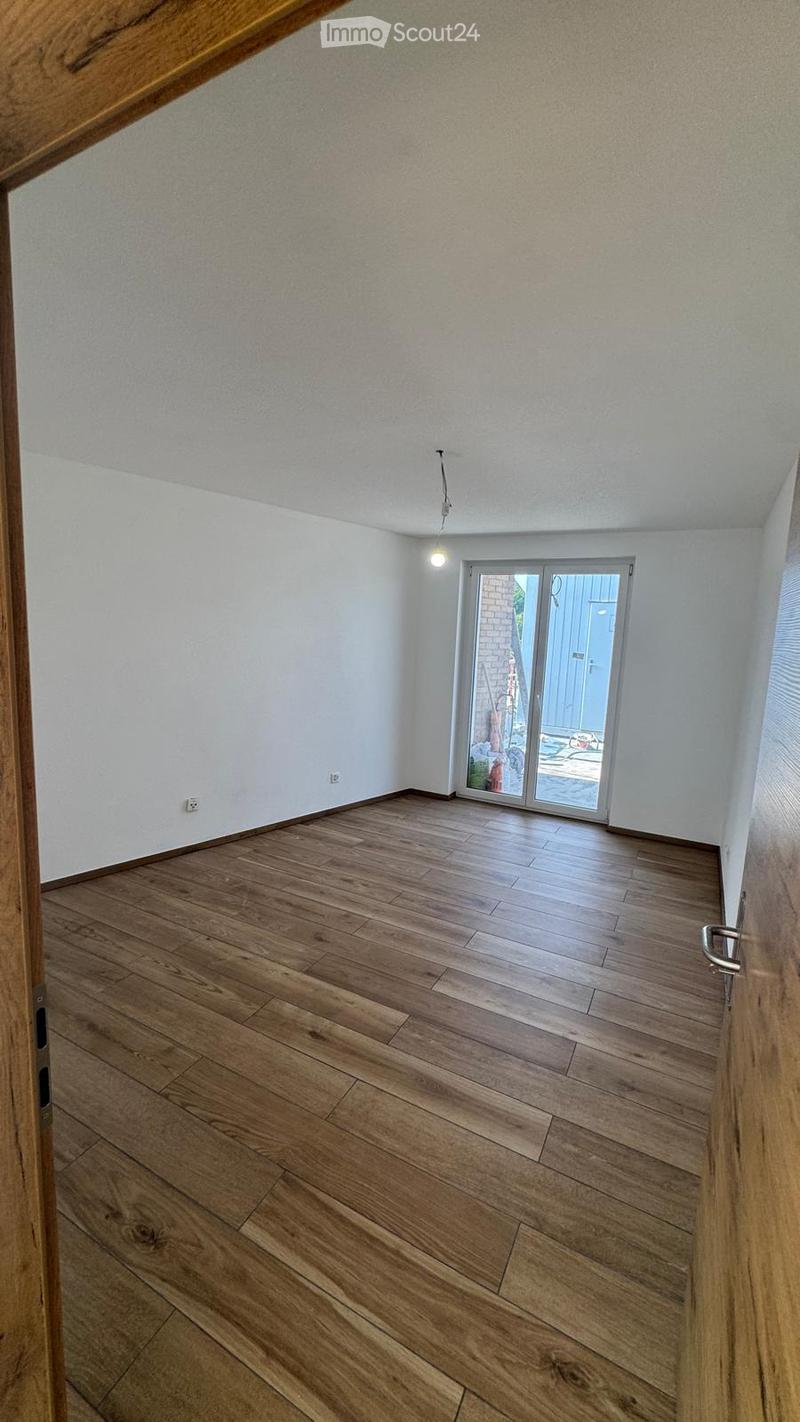 Empty room with wooden flooring, white walls, and a sliding glass door leading to an outdoor area.
