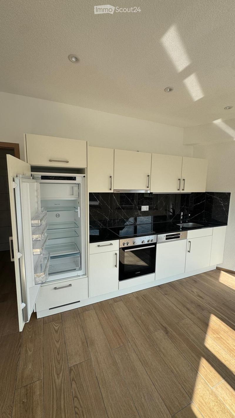 Modern kitchen with white cabinets, a stainless steel oven, a refrigerator, and a black countertop. The floor is made of light wood.