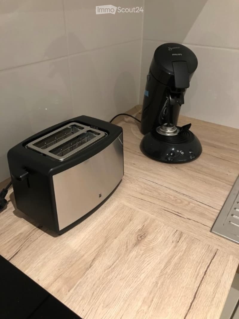 A modern kitchen countertop with a sleek black and silver toaster and a black coffee maker, both placed on a light wooden surface.