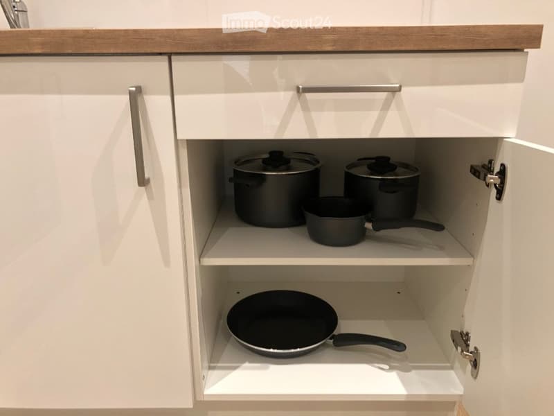 Open kitchen cabinet with white doors and silver handles, containing pots and pans neatly arranged on shelves.