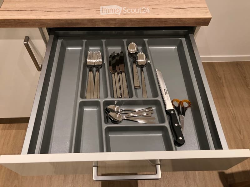 Open kitchen drawer with neatly organized cutlery including forks, knives, spoons, and scissors in separate compartments.