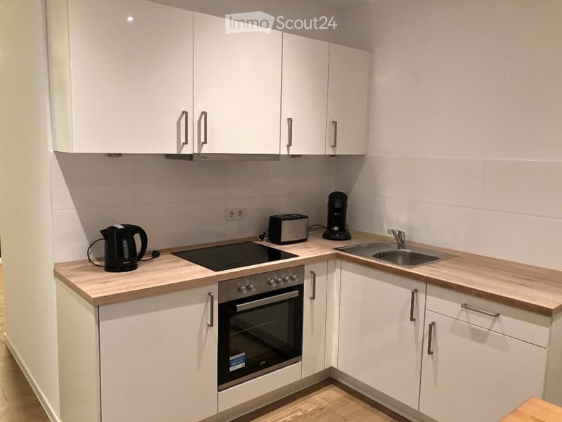 Modern kitchen with white cabinets, wooden countertops, and stainless steel appliances including an oven, sink, and faucet. A Keurig, toaster, and electric kettle are placed on the counter.