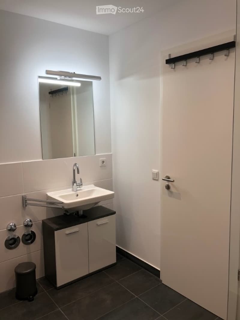 Modern bathroom with a white sink, mirror, and built-in cabinet. Features a sleek faucet and a dark tiled floor.
