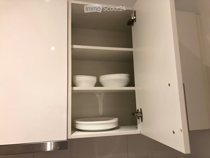 Open kitchen cabinet with white bowls and stacked plates on shelves.