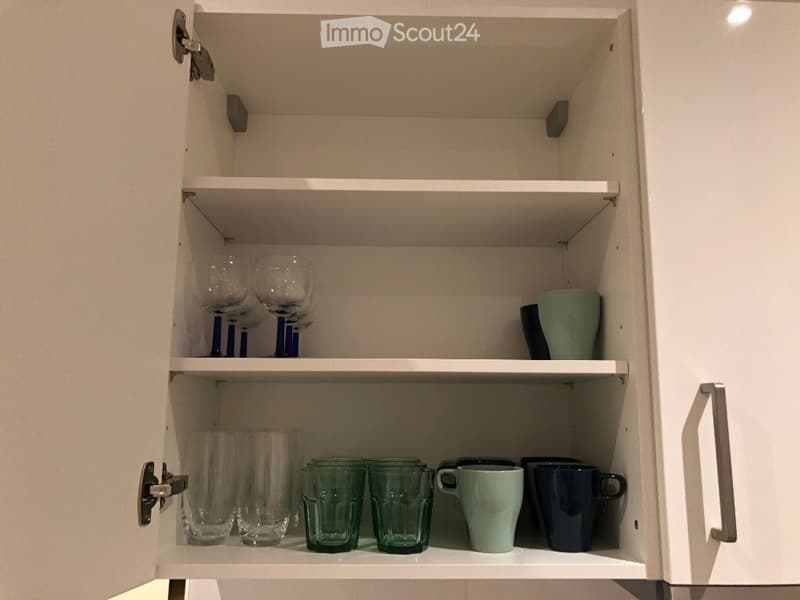 Open kitchen cabinet with multiple shelves displaying various cups and glasses neatly arranged.