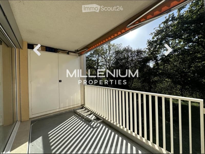 Balcony with white railing, tiled floor, and a view of trees and greenery.