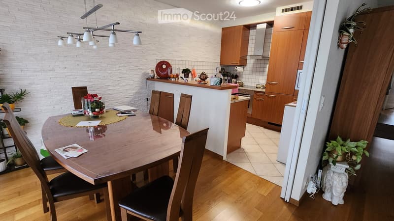 A modern kitchen and dining area with wooden cabinets, a round wooden dining table with chairs, and various kitchen appliances.