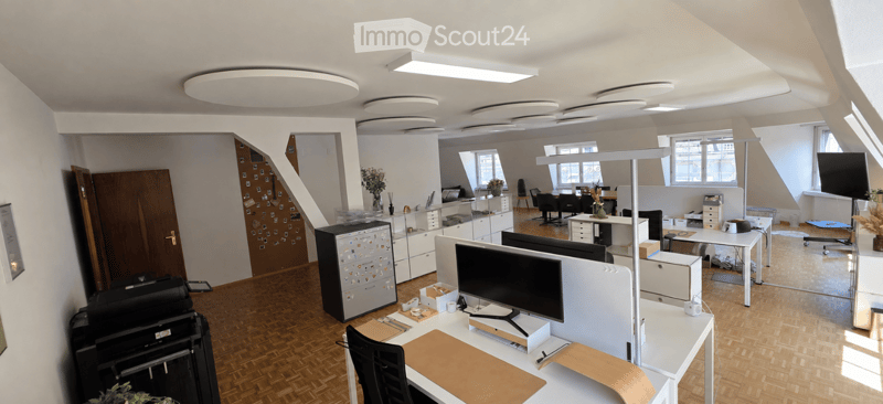 Modern office space with wooden flooring, multiple desks, chairs, computer screens, cabinets, and decorative vases.