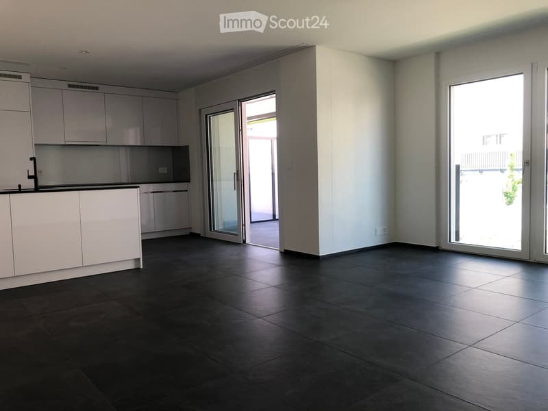 Empty kitchen with white cabinets, dark tiled floor, and large sliding glass doors leading to a balcony.