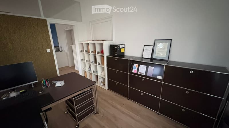 Office space with a desk, chair, computer monitor, keyboard, mouse, pen holder, cabinet, shelf, and framed certificates.