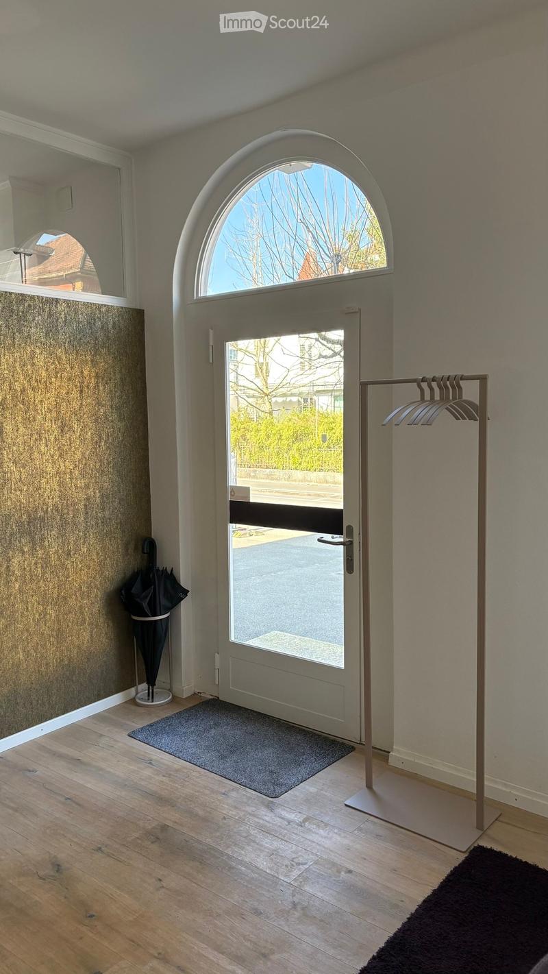Entrance hallway with wooden flooring, a large arched window above the door, a coat rack, and an umbrella stand.