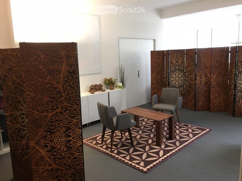 a room with desks, chairs, table, decorative items, rug and a screen