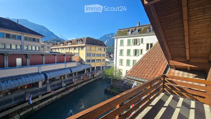Balcony overlooking a canal with surrounding buildings and mountains in the background.