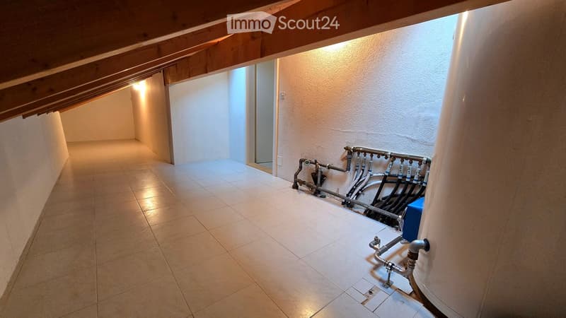 Clean, well-lit hallway with tiled flooring and exposed wooden beams on the ceiling. Plumbing pipes and a water heater are visible on one wall.