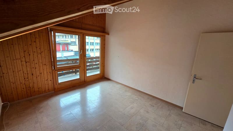 Empty room with tiled floor, wooden paneled wall, large window with wooden frame, and a door.