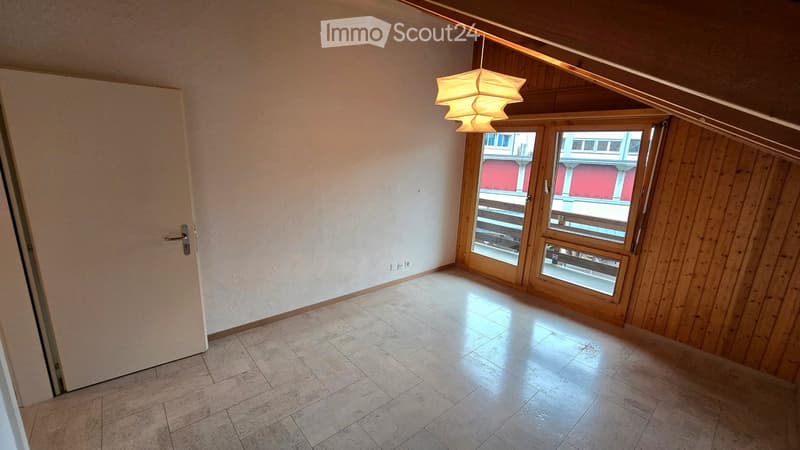Empty room with tiled floor, wooden walls, large window with view, and hanging light fixture.