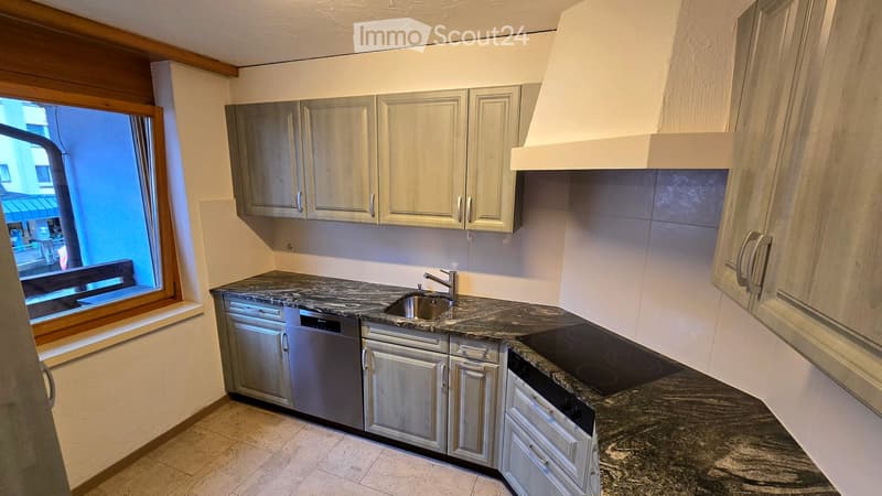Modern kitchen with grey cabinets, granite countertops, stainless steel appliances, and a window overlooking the street.