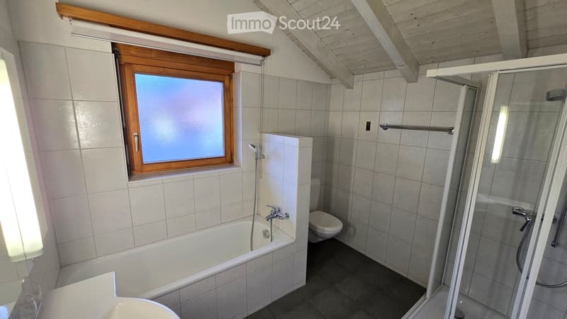 Modern bathroom with a bathtub, toilet, and walk-in shower. Features a large window with wooden frame and blinds, tiled walls, and a sleek design.