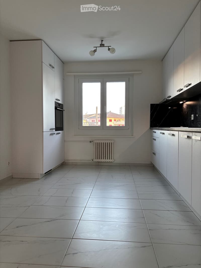 Empty kitchen with white cabinets, tiled floor, window, and radiator.