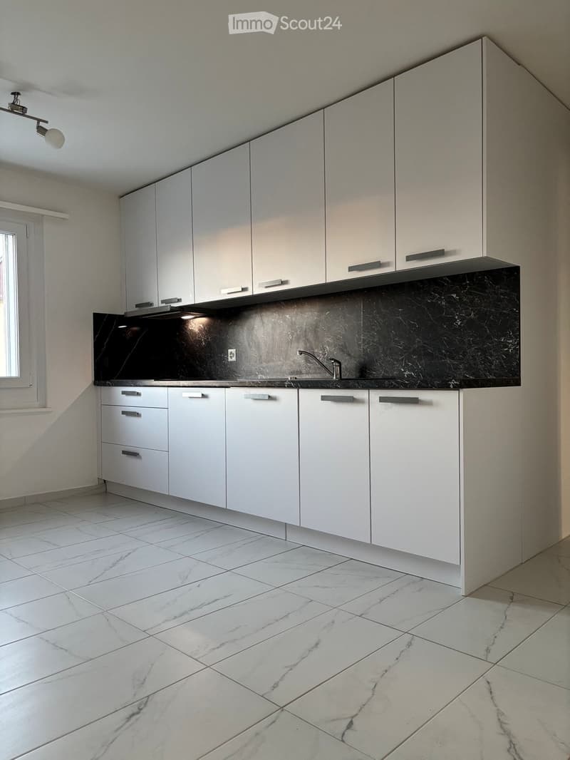 Modern kitchen with white cabinets, black marble countertops, and a sleek faucet. The floor is tiled with a marble pattern.