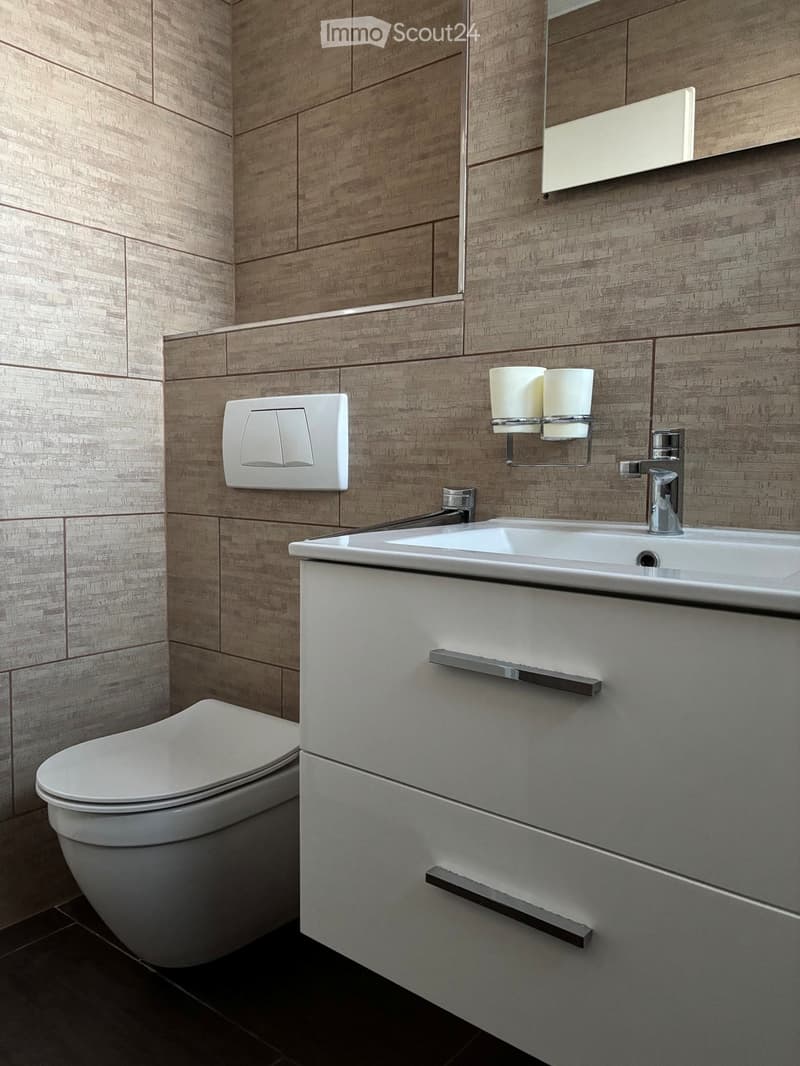Modern bathroom with a white toilet, sink, and mirror. The walls are covered in wood-textured tiles, and the sink has a sleek, contemporary design with a chrome faucet and a built-in cabinet.