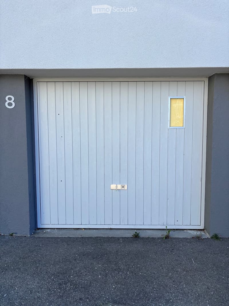 A closed garage door with a small window and a number "8" on the wall beside it.