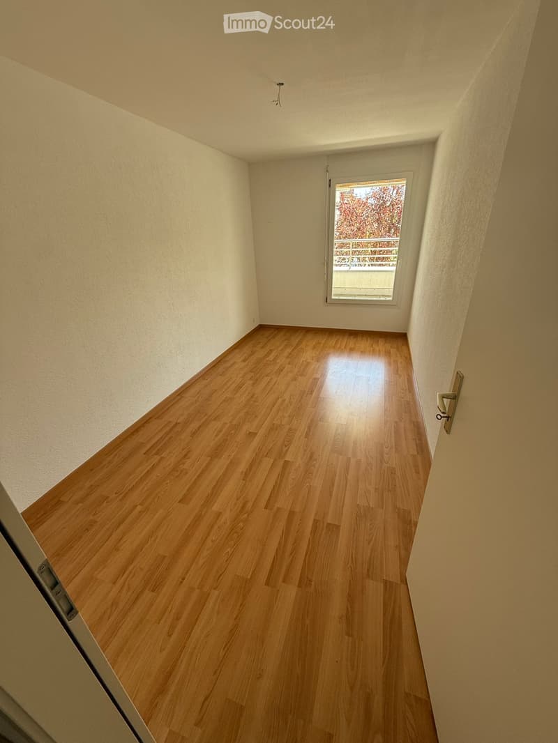 Empty hallway with wooden flooring, white walls, and a window at the end showing outdoor view.