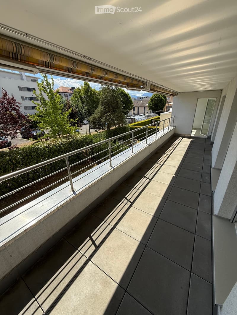 Balcony with tiled floor, metal railing, and view of greenery and buildings.