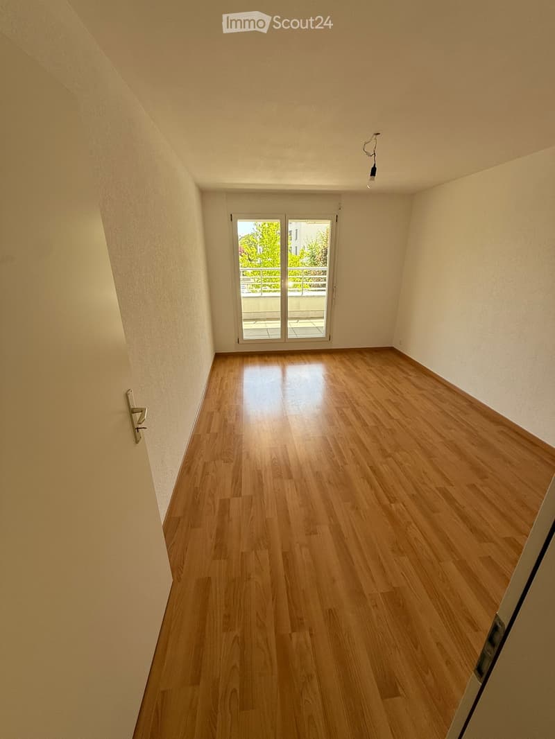 Empty room with wooden flooring, white walls, and a large window with a view of a balcony area.