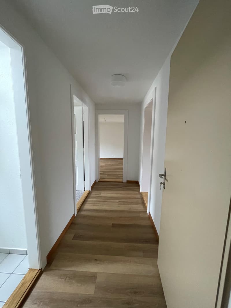 Empty hallway with wooden flooring, white walls, and several doors leading to other rooms.