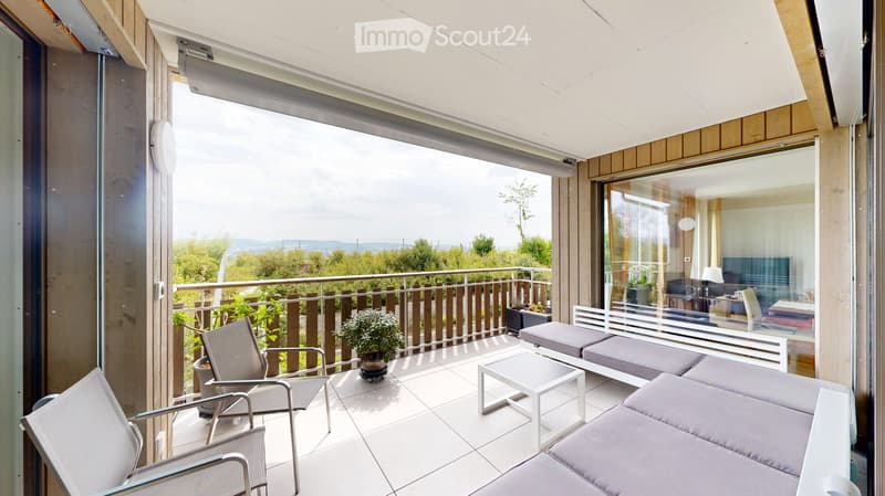 Modern balcony with white tiled floor, grey sofa, white chairs, small table, and potted plant, overlooking a scenic view.