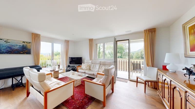 Bright living room with large windows and a balcony, featuring a white leather sofa, coffee table, armchairs, TV, and decorative items.