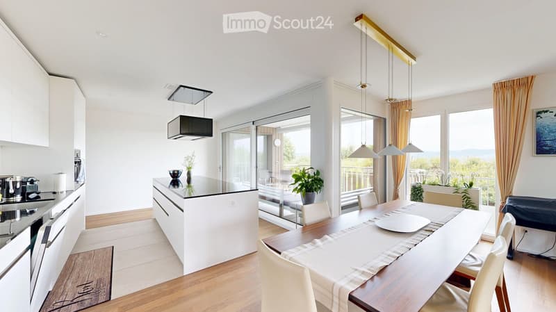 Modern open-plan kitchen and dining area with white cabinets, a central island, pendant lights, and large windows overlooking a balcony.