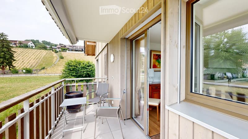 Balcony with a view of a green landscape, featuring a small table, two chairs, and a large flower pot.