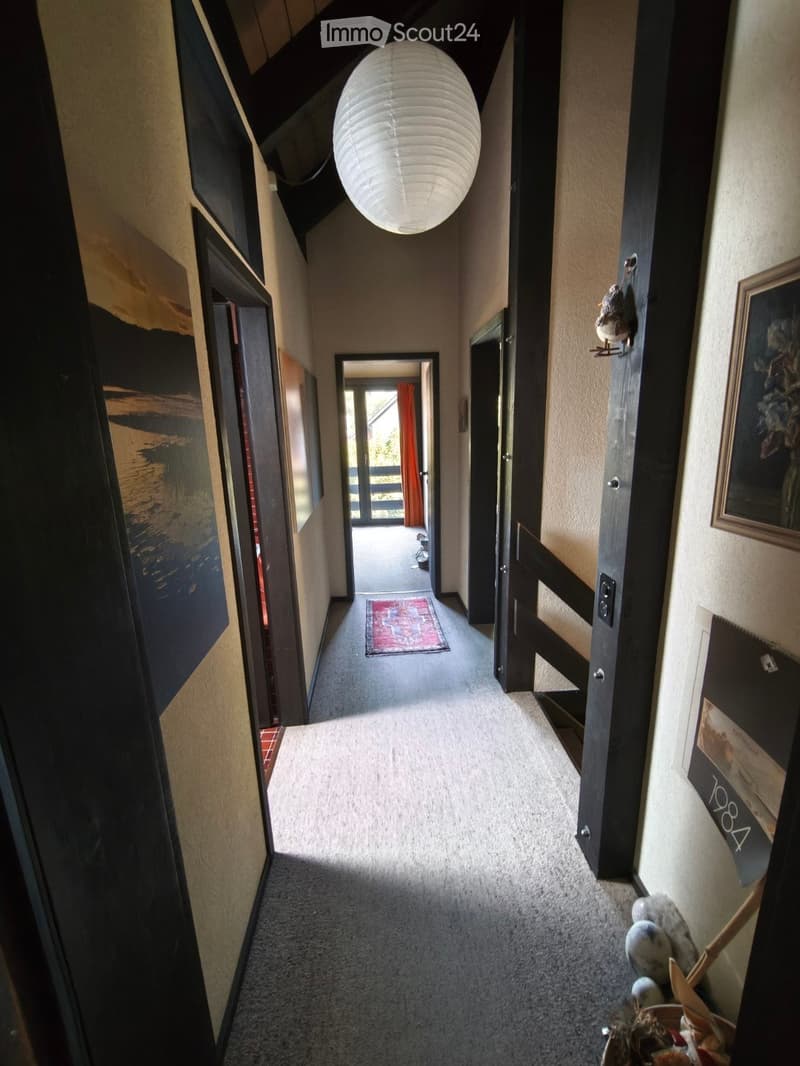 Carpeted hallway with a hanging lantern light fixture, several doors, and framed artwork on the walls.
