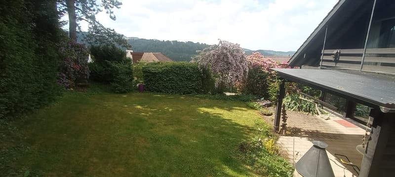 Well-maintained garden with a lawn, flowering shrubs, and a modern house with a covered patio area.
