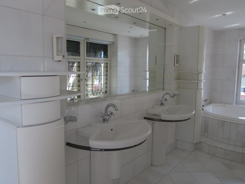 Modern bathroom with white tiles, large mirror, two sinks, bathtub, and white cabinetry.
