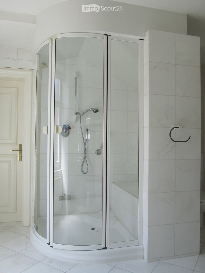 Modern bathroom with a glass walk-in shower, white tiled walls, and a shower bench.