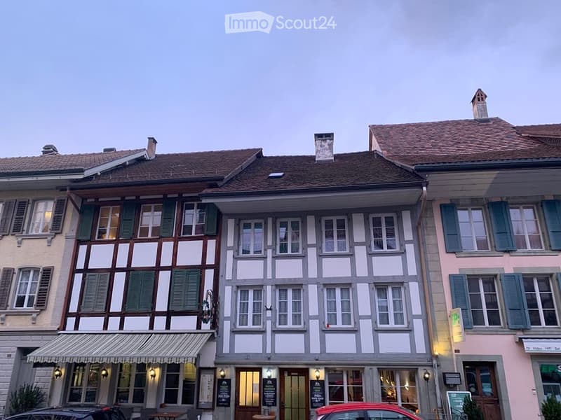 A row of traditional European townhouses with varied facades, including timber-framed and plaster designs, multiple windows, and awnings.