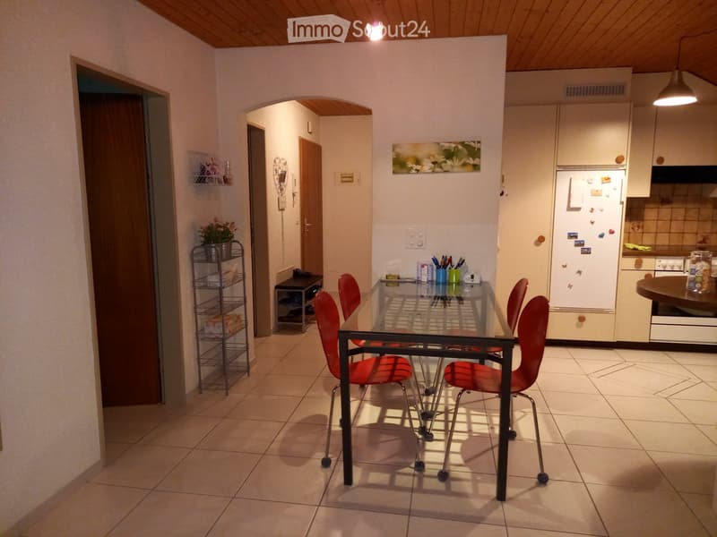 Modern kitchen with white cabinets, a glass dining table with red chairs, and a refrigerator with magnets.