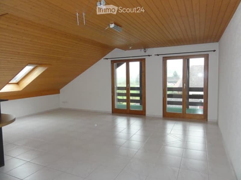 Bright, empty attic room with wooden ceiling, white walls, large skylight, and two sliding glass doors leading to a balcony.