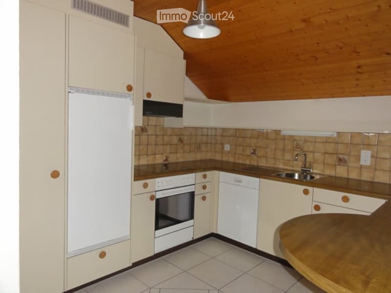 Bright kitchen with white cabinets, wooden accents, and modern appliances including a refrigerator, oven, and dishwasher. Features a wooden dining table and a sleek faucet over the sink.