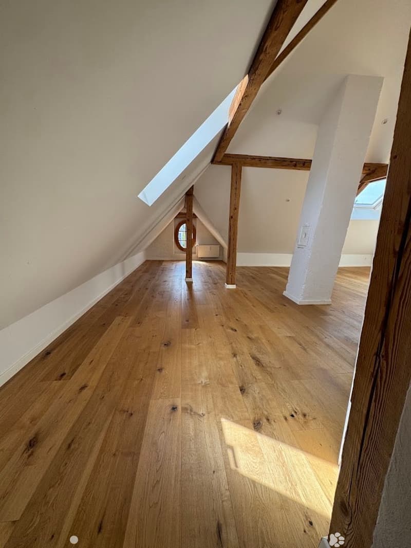 Empty attic space with wooden flooring, exposed wooden beams, and skylight windows allowing natural light.