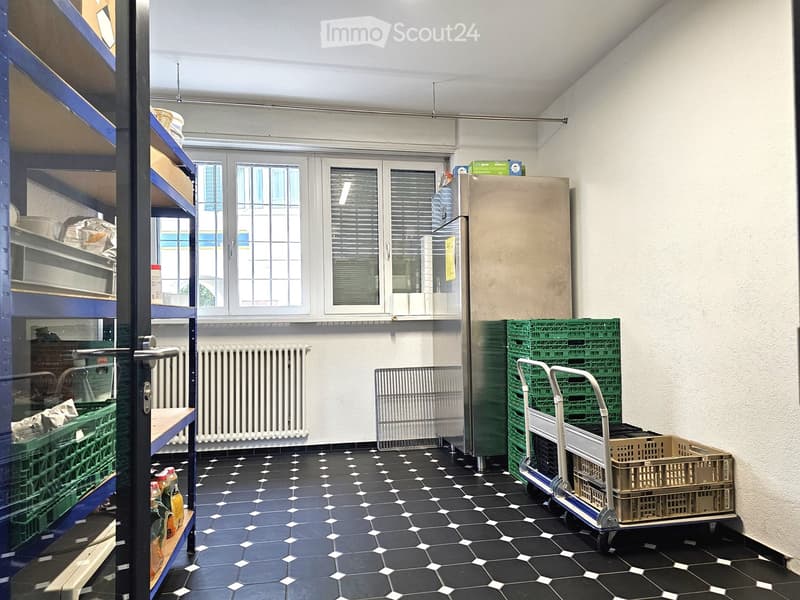A storage or utility room with black and white tiled floor, metal shelves, refrigerator, and green crates stacked on a cart.