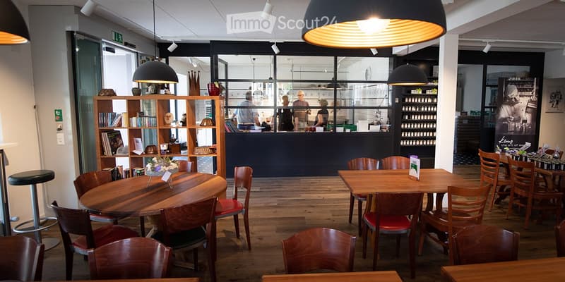 Modern restaurant interior with wooden tables, chairs, and shelves filled with books and decorative items.