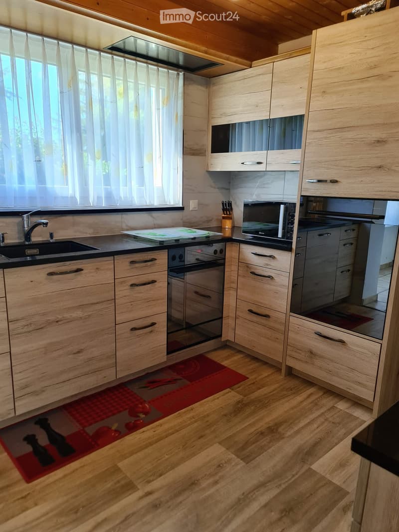 Modern kitchen with light wooden cabinets, stainless steel appliances, a black countertop, and a red rug on the floor.