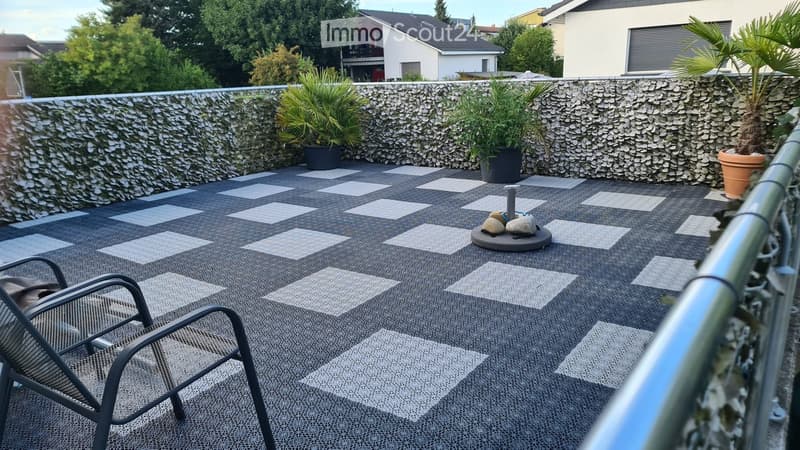 Balcony with checkered flooring, a metal chair, a small table with stones, and potted plants.