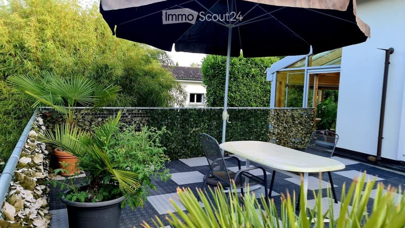 Garden area with a table, chairs, umbrella, potted plants, and a stone wall.