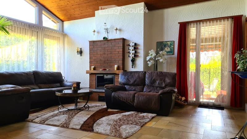Modern living room with a brick fireplace, two dark brown leather sofas, a coffee table, a wine rack, and large windows with sheer curtains.